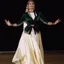 Placeholder: A graceful Azerbaijani female traditional dancer performing a famous Azerbaijani folk dance. She is wearing a beautiful traditional Azerbaijani dance costume: a long flowing silk dress with rich embroidery, wide skirt, and a colorful kelaghayi (traditional Azerbaijani silk headscarf) covering her head. The dancer moves elegantly with soft hand gestures, delicate finger movements, and smooth spinning steps typical of Azerbaijani women’s dances. The atmosphere is festive and cultural, with traditi