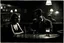 Placeholder: photo from an crisis of a couple in a bar. The scene is set in a dimly lit bar with a melancholic atmosphere, evoking a film noir style. The bar is filled with smoke and shadows, and with couples talking and drinking. At the bar counter, a man and a woman sit beside each other. The man is hold a glass beer and looking another young woman in bar, while the woman sadding face looking the counter. dramatic shadows, woman sadding face looking the counter. sadness, paint, loneliness