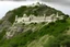 Placeholder: 'Junagarh Fort style', low grey granite fortress situated in wood covered Scottish Highlands seen from far away built at the top of grey granite cliffs