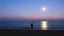Placeholder: A solitary figure stands on a tranquil beach under a twilight sky, illuminated by the moonlight reflecting on calm waters, creating a serene and contemplative atmosphere.