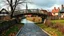 Placeholder: A stunning 3D render of a watercolor painting depicting a quaint rural scene during a rainy day. A cobblestone path winds towards a wooden bridge, which gracefully arches over a swollen creek filled with leaves. The village in the background boasts cozy houses and a stately church, casting elongated shadows under the overcast sky. The overall atmosphere is serene and atmospheric, capturing the essence of a peaceful, rain-soaked countryside., 3d render