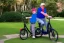 Placeholder: Photo of a single donald trump riding a Blue tricycle while wearing a pink polo shirt with the collar up