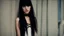 Placeholder: High resolution closeup in sharp focus of a beautiful and slender caucasian 18 year old teen girl with long black hair. She is wearing a black choker with her arms raided above her head. She is standing next to a wall gazing at the viewer.