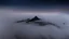 Placeholder: looking down from above at misty foreground and night sky background, no sun, single sharp narrow mountain peak coming through the mist in the center