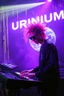 Placeholder: French cool synth player with crazy techno acid hair, he is called "Jean-Maurice Brûlée" performing at dance club, his name is "Jean-Maurice Brûlée" , white and purple Neon lights and purple smog, yellow shower rain, and "URINIUM" big sign on the wall, he is playing on synthesizers on stage with lot of laser beams and wearing black sunglasses, an earth is projected in background