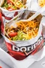 Placeholder: "Taco in a Bag" which consists of an open Doritos chip bag with sides rolled down, containing Doritos chips and cooked ground beef and lettuce and shredded cheese and chopped tomato pepper and onions and topped with more nacho chips, plastic fork, food blogger photography