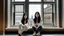 Placeholder: Two Asian women, around 22 years old, with long black hair, are sitting on a window sill inside a room with wooden floors and white walls. The window is large and rectangular, and it offers a view of a tall building with many windows. The building is made of light-colored brick or stone. The women are dressed in casual clothing, and one of them has her legs stretched out in front of her. There is a pair of shoes and a bag on the window sill next to them. The lighting is soft and diffused, and th