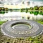 Placeholder: country side a calm lake ,a circular heavy plate with circle holes on it drops from distance in the lake water and splashes of water