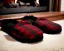 Placeholder: Red plaid slippers laying on a fur black rug by log cabin fireplace