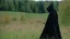 Placeholder: warrior in armor covered by black robe and hood in a field next to the forest