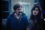 Placeholder: a young man and a beautiful woman standing next to each other, 1 9 8 0 s analog video, with mustache, small glasses, cold scene, out of focus background, house on background, the woman has long dark hair, photo realistic