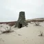 Placeholder: Fotografia di una ciminiera moderna brutalista, che sembra un tugurio, parzialmente sommersa. La struttura è erosa e inglobata dal paesaggio naturale, come se il tempo o l'ambiente avessero iniziato a "riassorbirla". L'atmosfera è desolata e surreale, con un ambiente circostante spoglio e sabbioso hasselblad h6d400c