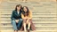 Placeholder: retro photo of a young couple in 70s style clothes sitting on the lower steps of the Danube stone embankment stairs in Budapest , the photo is old, stained and scratched in some places, one corner of the photo is missing, the girl's and the boy's faces are blurred and not clearly visible, behind them are many stairs