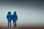 Placeholder: two people seen from behind walking side by side in an empty foggy plain with blue sky above