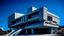 Placeholder: Imagen o ilustración de arquitectura brutalista de un(a) teatro y centro de artes escénicas, con una geometría caracterizada por volúmenes cúbicos interconectados por puentes. La superficie del edificio presenta concreto con acabado grabado al ácido. La escena está ambientada con una iluminación de cielo despejado azul profundo con contraste extremo, situada en un entorno de entorno de viñedos en terrazas con cantina brutalista. En el encuadre se aprecian detalles como muros curvados de guia de