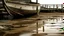 Placeholder: Detail of a pier or muddy beach, with subtle reflections and the boat as the main focal point.