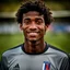 Placeholder: 85mm DSLR color photography of a very detailed headshot fitting all of head and hair in frame. 18-year-old French soccer player, and with no facial hair and has no facial hair, has short length straight black hair with a small smile, grey background