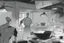 Placeholder: black and white storyboard, wide, on the Foreground there is a man and in the background, 3 chefs, scattered throughout the kitchen cooking, frying, cutting