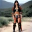 Placeholder: youthful Caroline Munro in a native outfit, she wears leather boots