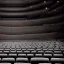 Placeholder: a single chair on stage in spotlight close up view facing empty audience at a dark and empty symphony hall