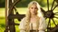 Placeholder: Photo is in sharp focus with high resolution and is a closeup of a beautiful and slender caucasian 16 year old teen girl with long wavy platinum blonde hair. She is wearing a medieval peasant dress with a coset. She is seated at a spinning wheel gazing at the viewer.