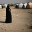 Placeholder: A Palestinian woman wearing the Palestinian dress carries her dead son as she screams and cries at night, with explosions in refugee tents behind her.