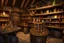 Placeholder: inside of a medieval shop, wooden walls, log pillars, stone bar with shop keeper behind it, magical ingredients on display and weapons on display. people, elves, goblins, orcs, dwarves and lizard folk in room. low lighting and creatures in containers. shelves half empty