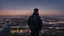 Placeholder: An Englishman in a bomber jacket standing to one side of a tall building looking across a city after sunset