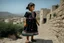 Placeholder: A five-year-old Palestinian girl wearing a traditional dress and new shoes looks to the side and points at a distant building.