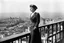 Placeholder: The famous photo of Marina Ginestà, taken by Juan Guzmán on July 21, 1936, captures a striking moment during the early days of the Spanish Civil War. In the image, Ginestà stands confidently atop the Hotel Colón in Barcelona, a backdrop of the city visible behind her. She is dressed in a stylish military outfit, a symbol of her involvement in the anarchist movement. Her posture is assertive, with one hand resting on a wall and the other holding a rifle, embodying both strength and defiance.