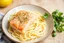 Placeholder: A plate of pasta with a piece of salmon on top. The salmon is seasoned with herbs and spices. The pasta is cooked and served in a bowl