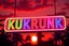 Placeholder: A 1980 disco sign labeled "KUKRUNK" bold multi colored 80s font, miami vice background drop, sunset