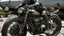 Placeholder: Una moto cuyas ruedas son anillos de vértebras ensartadas, el bloque motor late bajo una cúpula de costillas abiertas, y a su lado, un jinete con mono de látex agrietado y un casco de vendas que gotean aceite negro.
