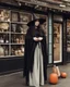 Placeholder: full-length, young woman dressed like a modern-day witch, with dark hair, outside a shop