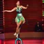 Placeholder: a very beautiful lady with makeup and bub hair, wearing a pretty blue-green sports pants an top, shows her performance driving a circus single Wheel monoBike in a modern stage with metallic fractal recursive structures that animate, and dynamic color lights.camera zoom to full body all time
