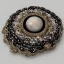 Placeholder: rose ivory brooch with black pearl inlay, opalescent marble carving, decorative design, classical ornament, highly ornate, highly intricate, highly detailed etching, marble carving, warm lighting, linen backdrop