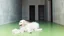 Placeholder: A woman with ash-blonde hair sits on the bright green floor of a concrete room, petting a long-haired white dog. The room has a minimalist aesthetic with light concrete walls and dark openings leading to other areas.