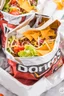 Placeholder: "Taco in a Bag" which consists of an open Doritos chip bag with sides rolled down, containing Doritos chips and cooked ground beef and lettuce and shredded cheese and chopped tomato pepper and onions and topped with more nacho chips, food blogger photography