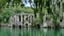 Placeholder: A ruined stone building in a lake, balconies, verandas, arches, bridges, spires, stairs, trees, dense foliage, spanish moss, ivy, blue sky, white clouds