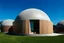 Placeholder: A sleek, minimalist dome home designed from monolithic concrete, where the main dome has a metallic finish and the smaller domes have wood-clad exteriors. The combination of materials creates a futuristic yet inviting aesthetic.