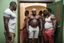 Placeholder: group of big stocky black muscular men from Niger , tank top, bulging shorts, inside a modest living room, queuing in front of the door of a room