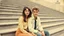 Placeholder: retro old photo of a young couple in 70s style clothes sitting on the lower steps of the Danube embankment, the photo is old, stained, scratched in some places, the girl's and the boy's faces are blurry and not clearly visible, behind them are stairs