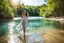 Placeholder: beautiful girl in pretty dress walking in water toward camera in trees next to wavy river with clear water and nice sands in floor.camera capture from her full body front