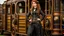 Placeholder: full-length portrait of a pale-faced steampunk woman with auburn wavy shoulder-length hair, with detailed metal arms and legs, dressed in leather trousers, and a jacket, standing beside a steam carriage