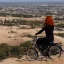 Placeholder: do topo de uma colina, uma jovem ruiva observa motocicletas indo em direção a uma grande cidade tecnológica em um terreno arenoso