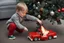 Placeholder: A crying toddler takes a burning car out of a LEGO box marked Land Rover next to the Christmas tree.