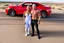 Placeholder: make a pic with short hair and little bald bodybuilder Knut Spildrejorde from Norway and his fitness wife Jeanette, they are standing front of his new red car Chevrolet Camaro, very busy highway in sunny desert Texas in the background