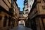 Placeholder: Old English Tudor Alley with shops, signs, bridges, and balconies, sunny day, warped and grubby