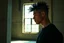 Placeholder: half portrait, a young cyberpunk man in black shirt with a mohawk standing in a large room with a window, man's short dark hair with shaved sides, partially visible face, dramatic light and shadows, shadow cast on a concrete pillar, dynamic hair movement, cinematic, dynamic, dramatic, amazing reflections, excellent shadows, perfect contrast, filmstill, behind bars, profile, side view, worn and textured walls, muted green and beige color tones, kpop style colors, industrial setting, tall concret