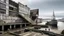 Placeholder: Un edificio cultural junto a un puerto industrial abandonado, ensamblaje asimétrico de acero oxidado, madera envejecida y hormigón crudo, geometrías no ortogonales y estructuras tensadas que parecen desplazarse como un organismo vivo, pequeñas embarcaciones y gaviotas alrededor, personas recorriendo rampas y vacíos intermedios abiertos al mar, sensación de arquitectura inacabada y narrativa, iluminación gris atlántica, estilo gráfico de collage constructivista combinado con g